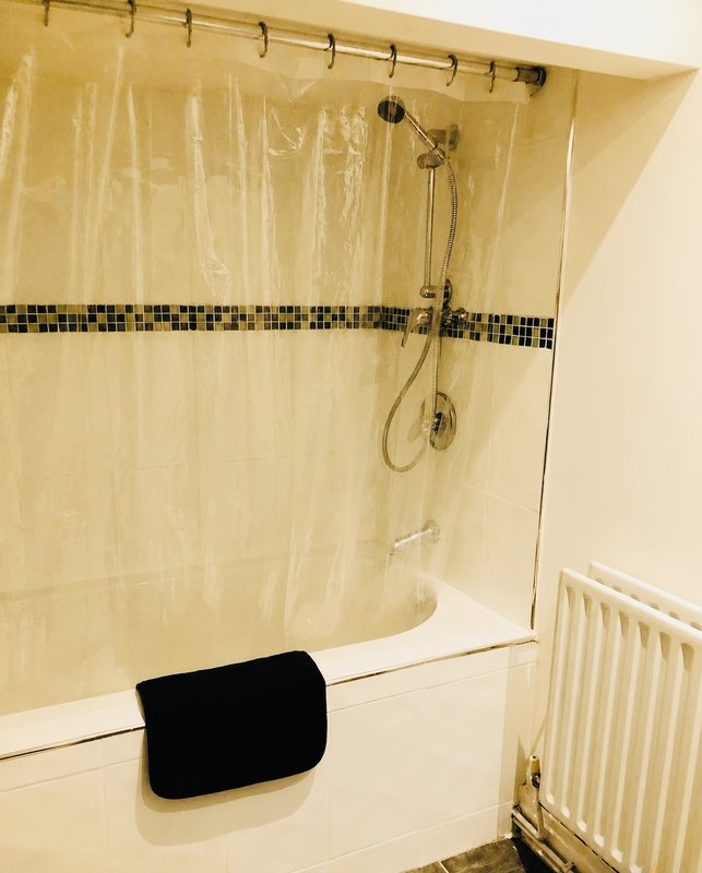Bathroom with shower enclosure, cream tiles, black towel and radiator