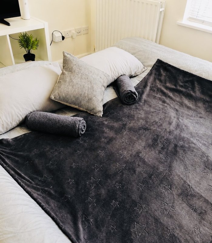 Bedroom with double bed, white pillows, textured cushions and dark throw blanket
