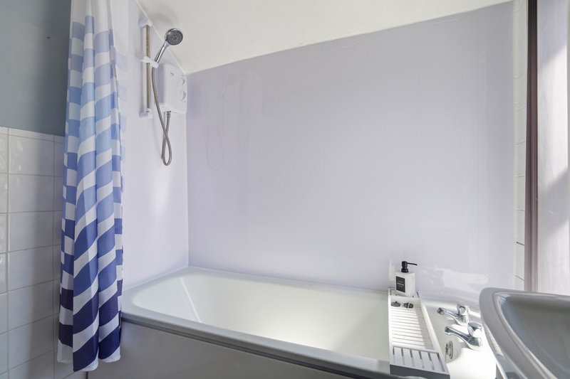 Bright bathroom with white bathtub, blue checkered shower curtain, and wall-mounted showerhead