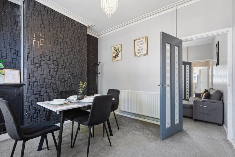 Modern dining area with white table, black chairs, geometric wallpaper, and crystal chandelier