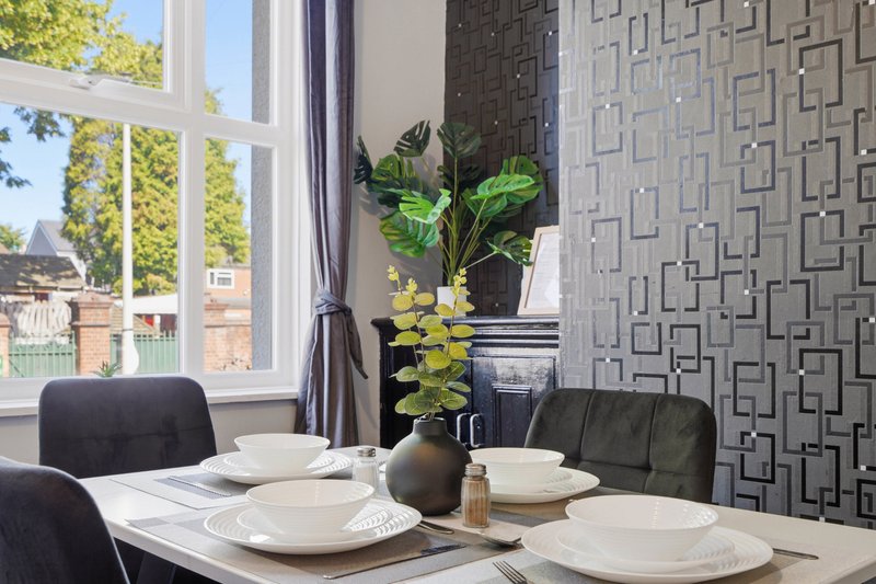 Dining room with white table, black chairs, place settings, potted plants and large window