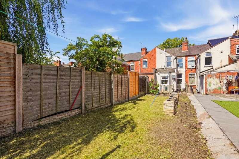 Outdoor garden space with wooden fence, lawn, patio and brick terraced houses