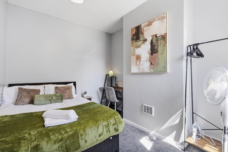 Bedroom with double bed, green bedding, framed artwork, desk chair, and floor fan