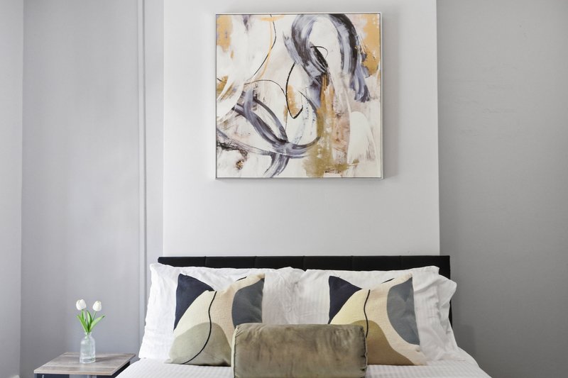 Modern bedroom with black bed frame, white bedding, decorative pillows, and abstract wall art.