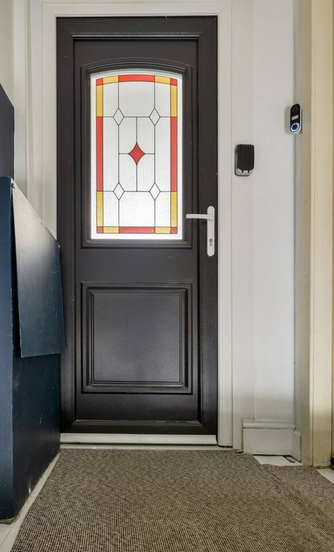 Black exterior door with stained-glass panel and brass handle, entry hallway with carpet flooring