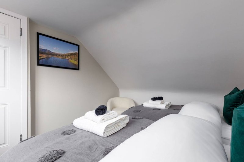 Attic bedroom with double bed, white pillows, folded towels, wall-mounted TV and green cushion