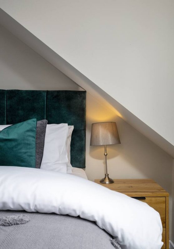 Attic bedroom with double bed, teal velvet headboard, bedside lamp and sloped ceiling