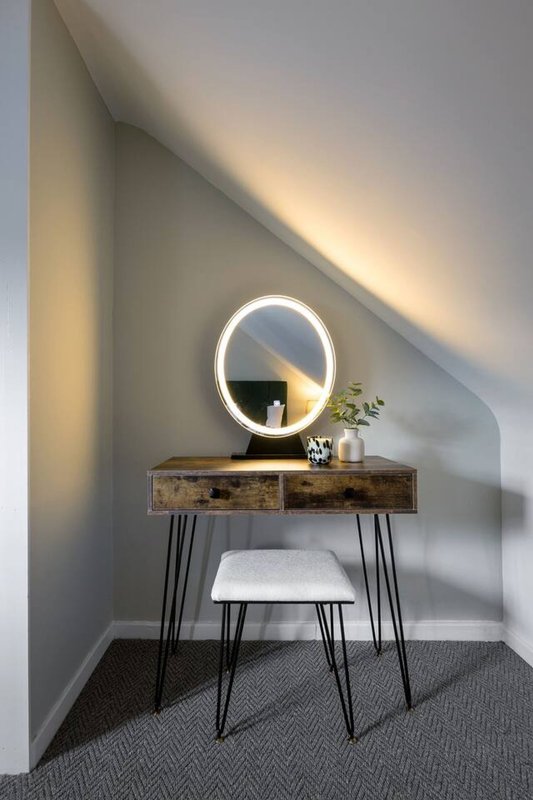 Bedroom vanity area with round illuminated mirror, wooden desk, metal legs, and stool