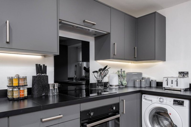 Modern kitchen with gray cabinetry, black countertop, integrated appliances and white washing machine