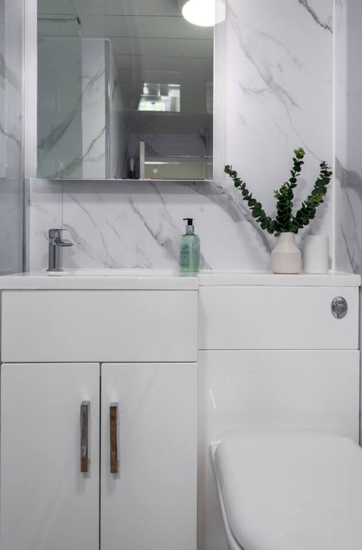Modern bathroom with white marble vanity, mirror, sink, and potted plant decoration