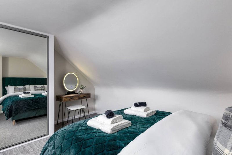 Modern attic bedroom with white bed, teal quilted throw, round mirror and ensuite visible