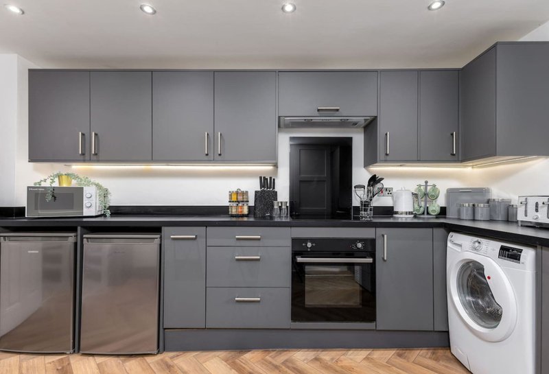 Modern kitchen with grey cabinetry, stainless steel appliances, black countertop and white washing machine