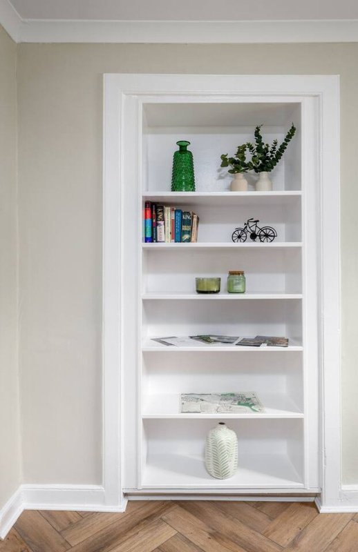 Built-in white shelving unit with decorative items, books, plants, and glassware displayed across six shelves
