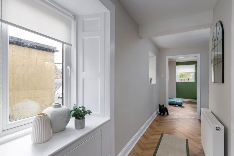 Bright hallway with white walls, wooden flooring, potted plant on windowsill, and open doorways