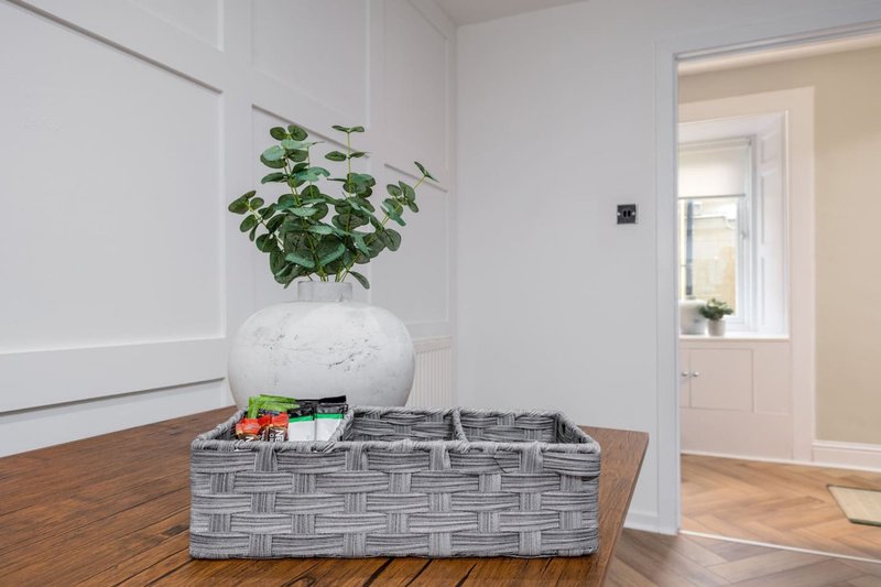 Bright entryway with wooden floor, white vase with green plant, and woven storage basket