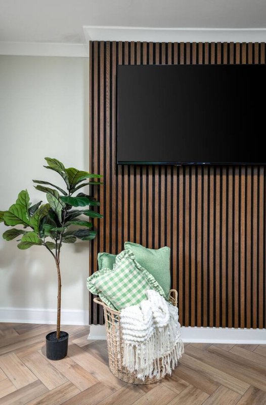Modern bedroom corner with potted plant, wicker chair, folded blankets and wooden wall paneling