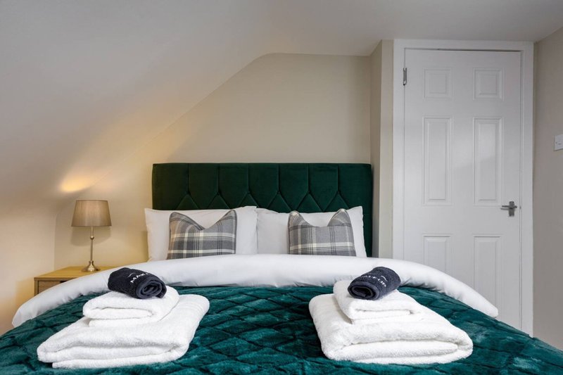 Bedroom with twin beds, green headboard and duvet, white pillows and folded towels