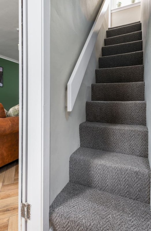 Staircase with gray carpet, white handrail, and view into adjacent room with green wall