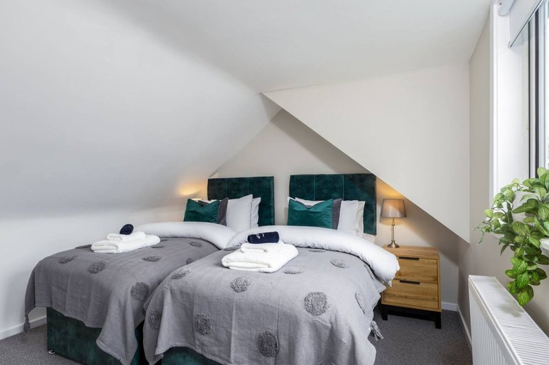 Attic bedroom with double bed, green velvet headboard, white bedding and wooden side tables