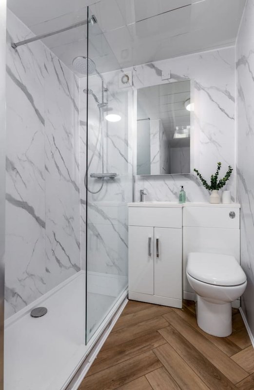Modern bathroom with marble shower enclosure, white vanity, toilet and wooden floor