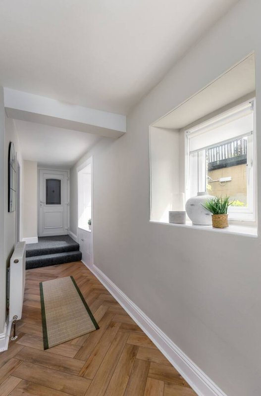 Bright hallway with herringbone wood flooring, white walls, window with potted plant, and modern pendant lighting