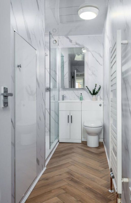 Modern bathroom with white vanity, toilet, shower enclosure and herringbone wood flooring