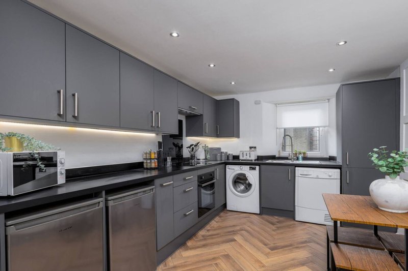 Modern kitchen with dark grey cabinets, black countertops, stainless steel appliances and wooden dining table