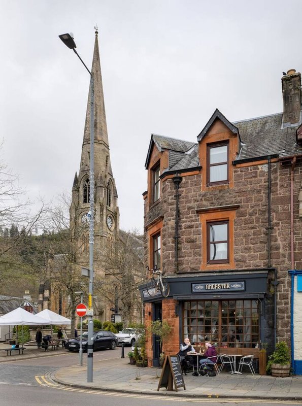 Stone church with tall spire next to brick buildings on village street corner