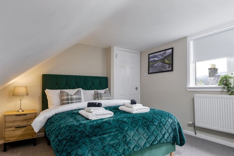 Bedroom with teal quilted bed, wooden headboard, bedside lamp, and window with radiator