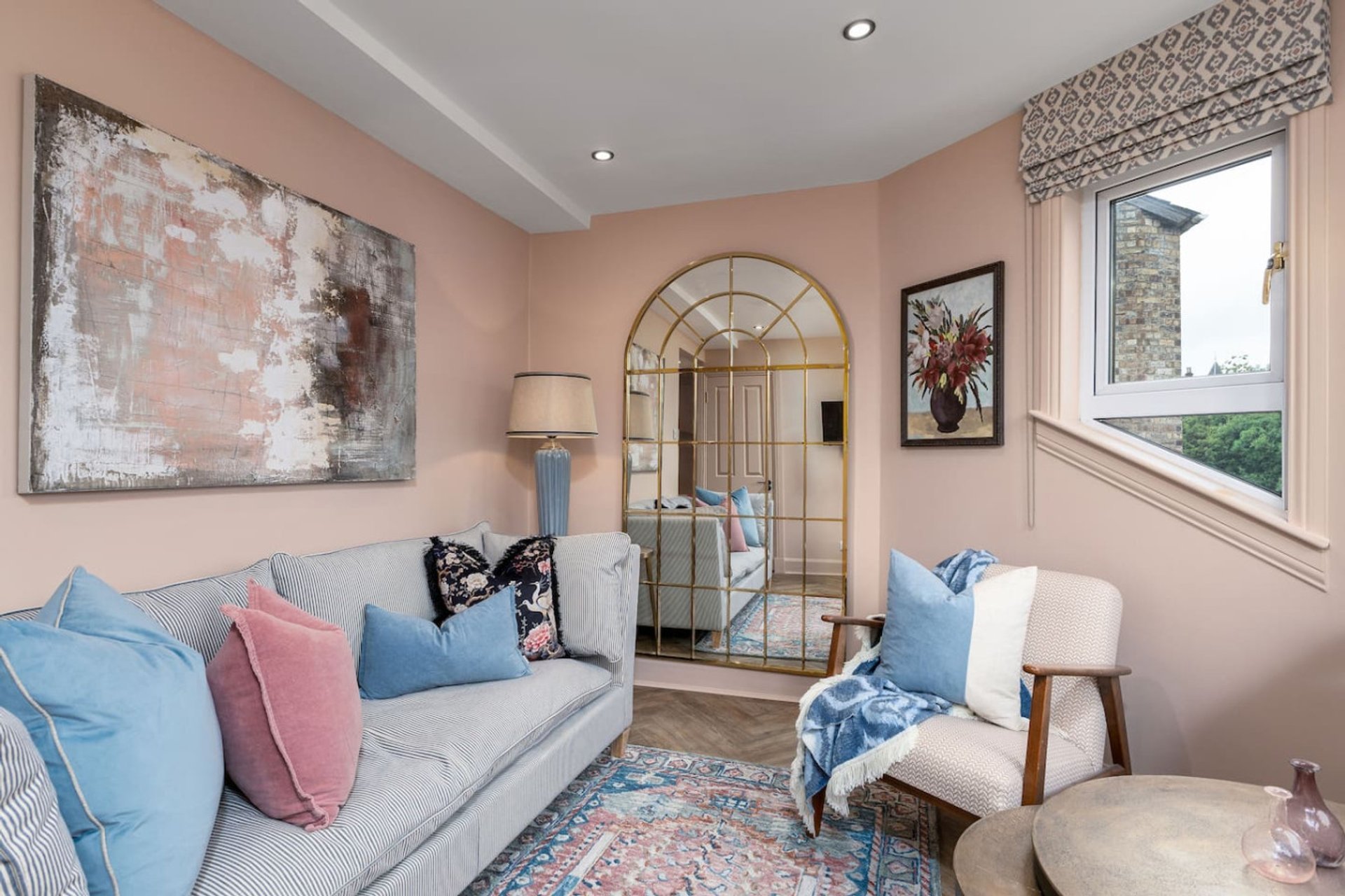Bright living room with grey sofa, pink and blue cushions, arched mirror and framed artwork