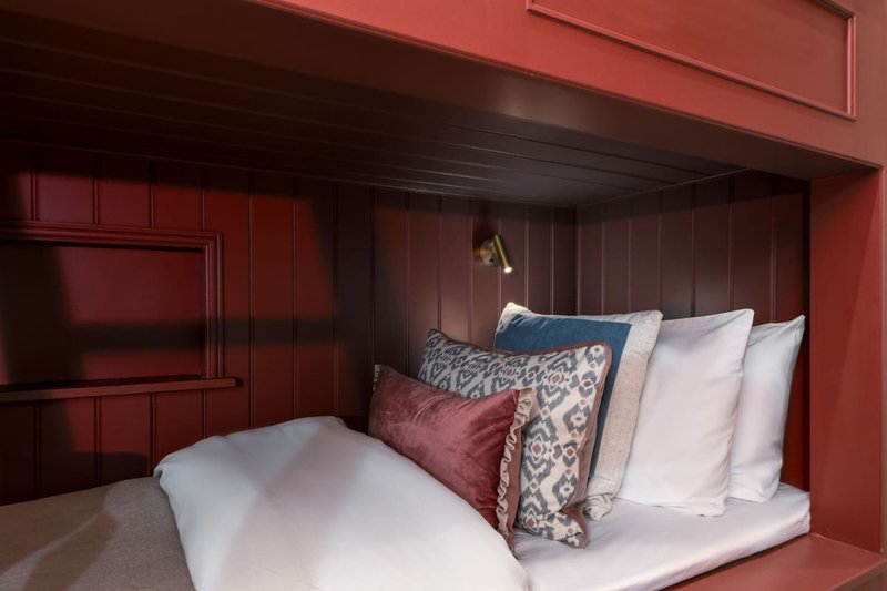 Modern bedroom with burgundy panelled walls, double bed with patterned cushions and white pillows