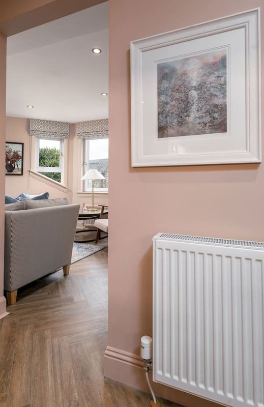 Pink hallway with white radiator, framed landscape artwork, and open doorway to living area