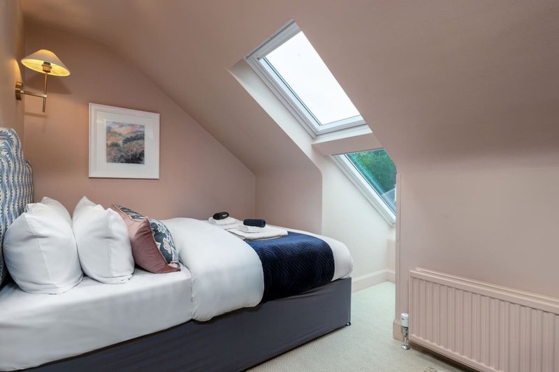 Attic bedroom with double bed, white pillows, skylight window and framed landscape art