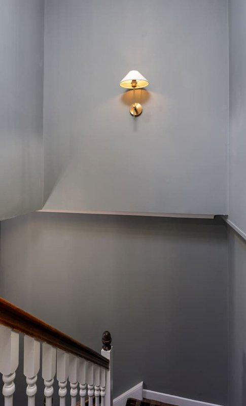 Stairwell with white balustrade, two-tone grey walls, and brass wall light fixture