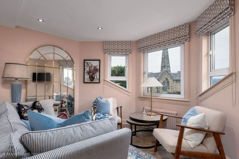Bright living room with blue sofa, armchair, arched mirror and large windows overlooking garden