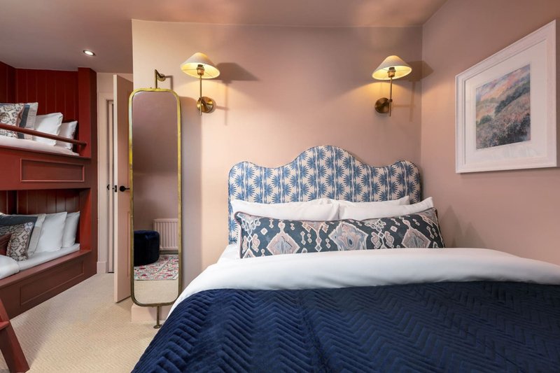 Bedroom with blue patterned headboard, white bedding, dark blue duvet, wall lamps and framed artwork