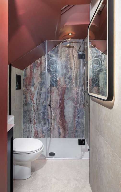 Modern bathroom with walk-in shower, glass enclosure, toilet, and burgundy walls