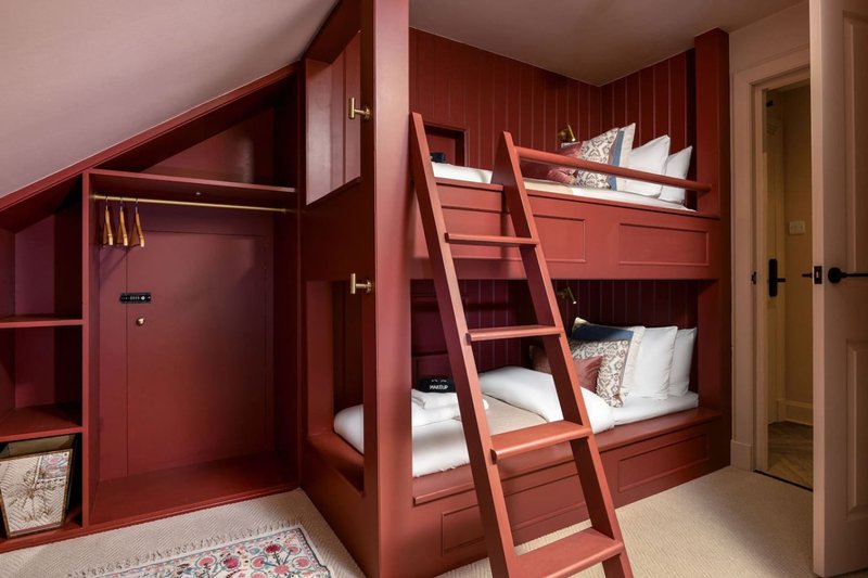 Children's bedroom with red bunk beds, ladder, built-in storage shelves and wooden floor