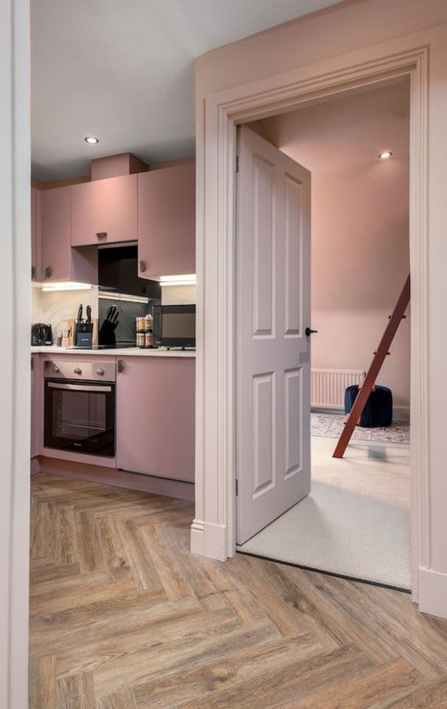 Modern kitchen with pink cabinetry, wooden flooring, and open doorway to hallway