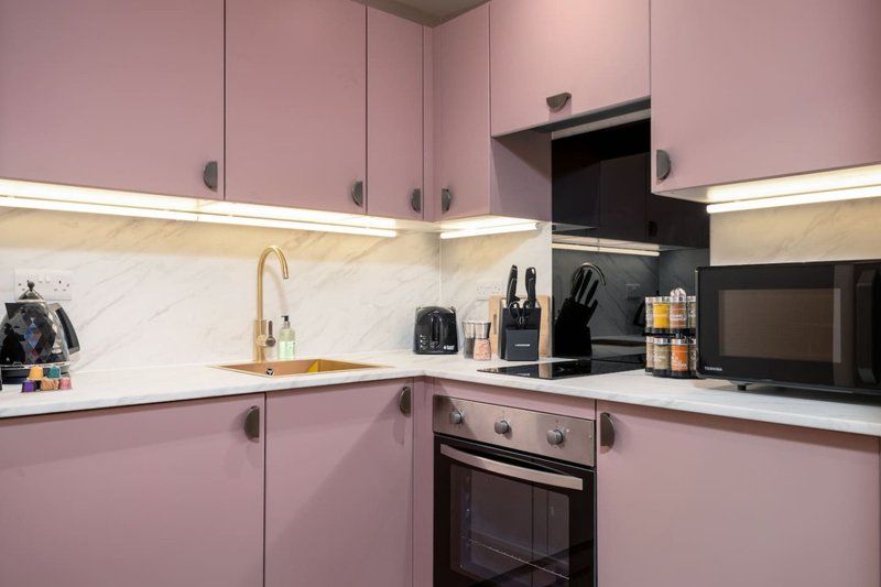 Modern kitchen with pink cabinetry, marble backsplash, built-in appliances and countertop accessories