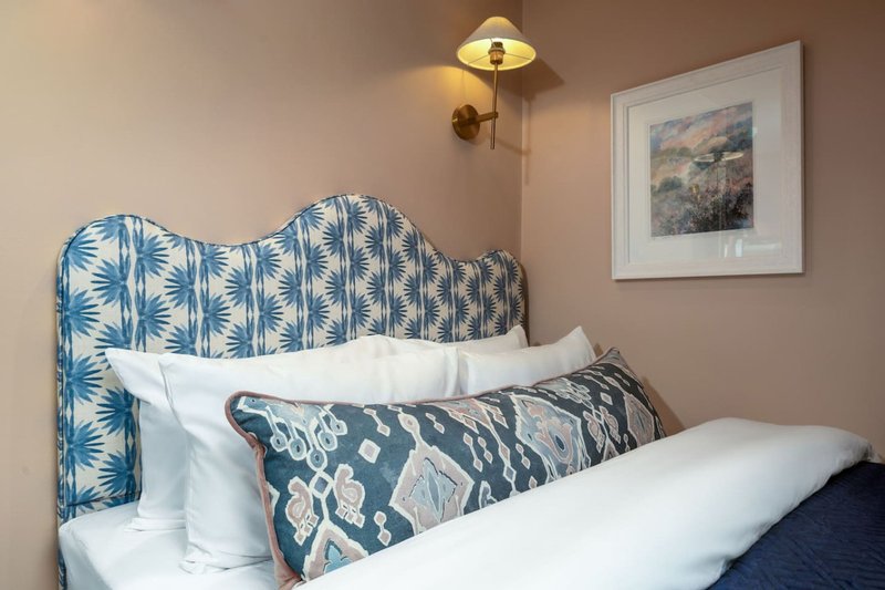 Bedroom with blue patterned headboard, white pillows, decorative cushion and wall-mounted lamp