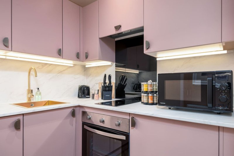Modern kitchen with pink cabinetry, white countertop, integrated appliances and pendant lighting