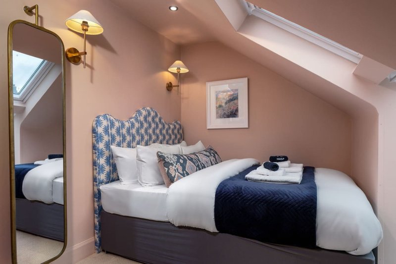 Attic bedroom with double bed, blue patterned headboard, white bedding, brass wall sconces and skylight