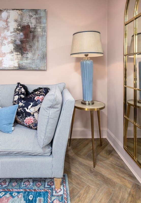 Light pink bedroom with upholstered sofa, decorative pillows, table lamp, and abstract wall art