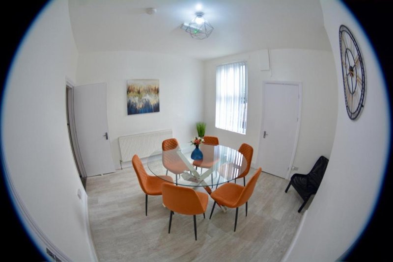Bright dining room with glass table, orange chairs, wall art and clock