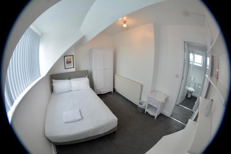 Small bedroom with single bed, white wardrobe, and dark carpeted floor under sloped ceiling