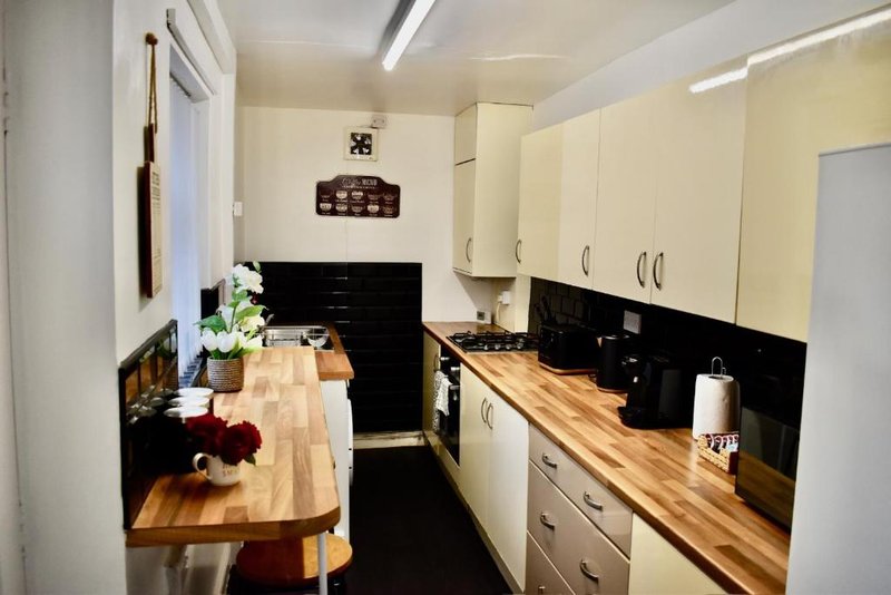 Galley kitchen with cream and black cabinetry, wooden countertops, and dining counter with stools