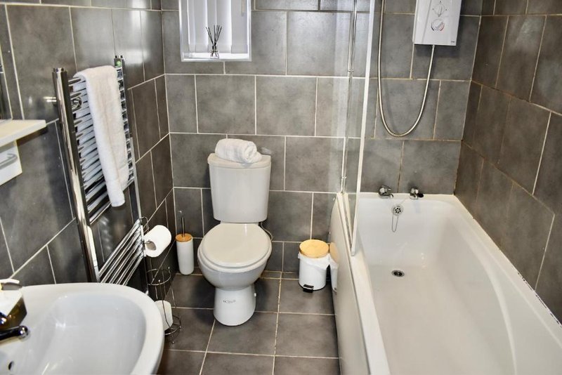 Modern bathroom with grey tile walls, toilet, bathtub, sink and heated towel rail