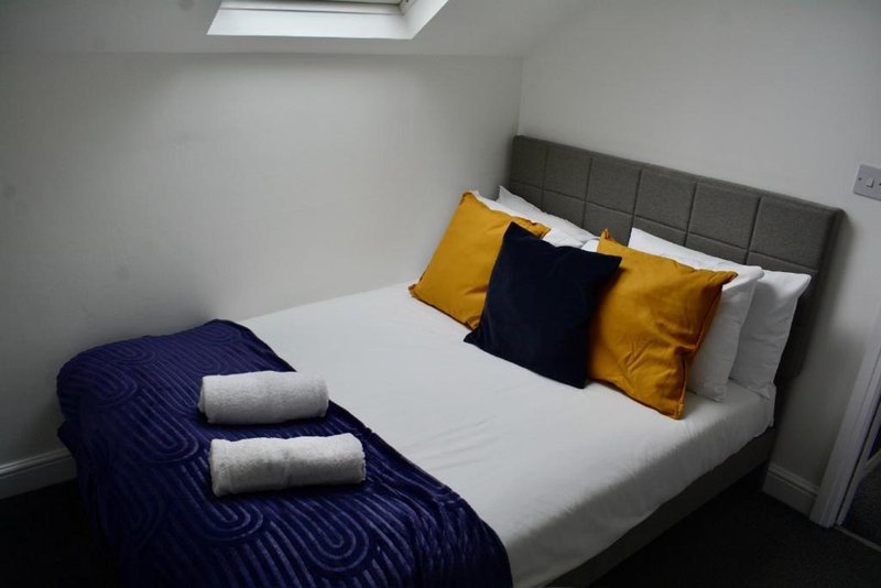 Modern bedroom with double bed, grey headboard, yellow and navy cushions, skylight window