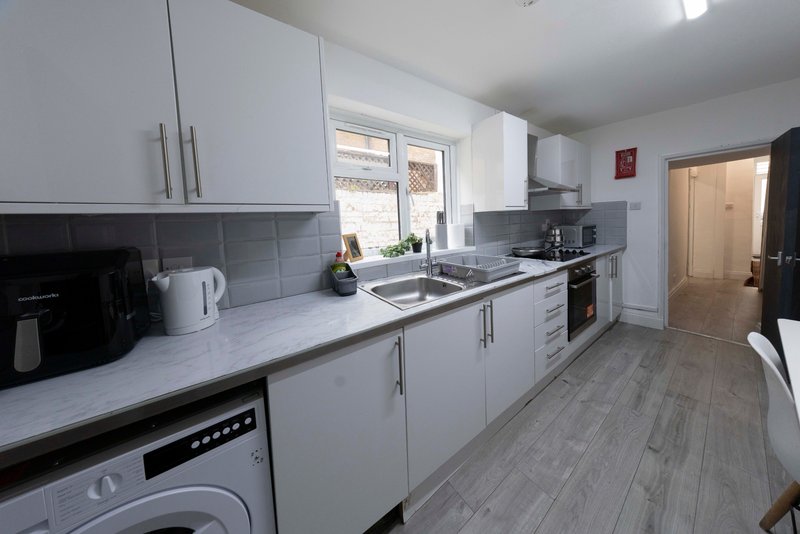 Modern kitchen with white cabinetry, gray tile backsplash, stainless steel appliances and window